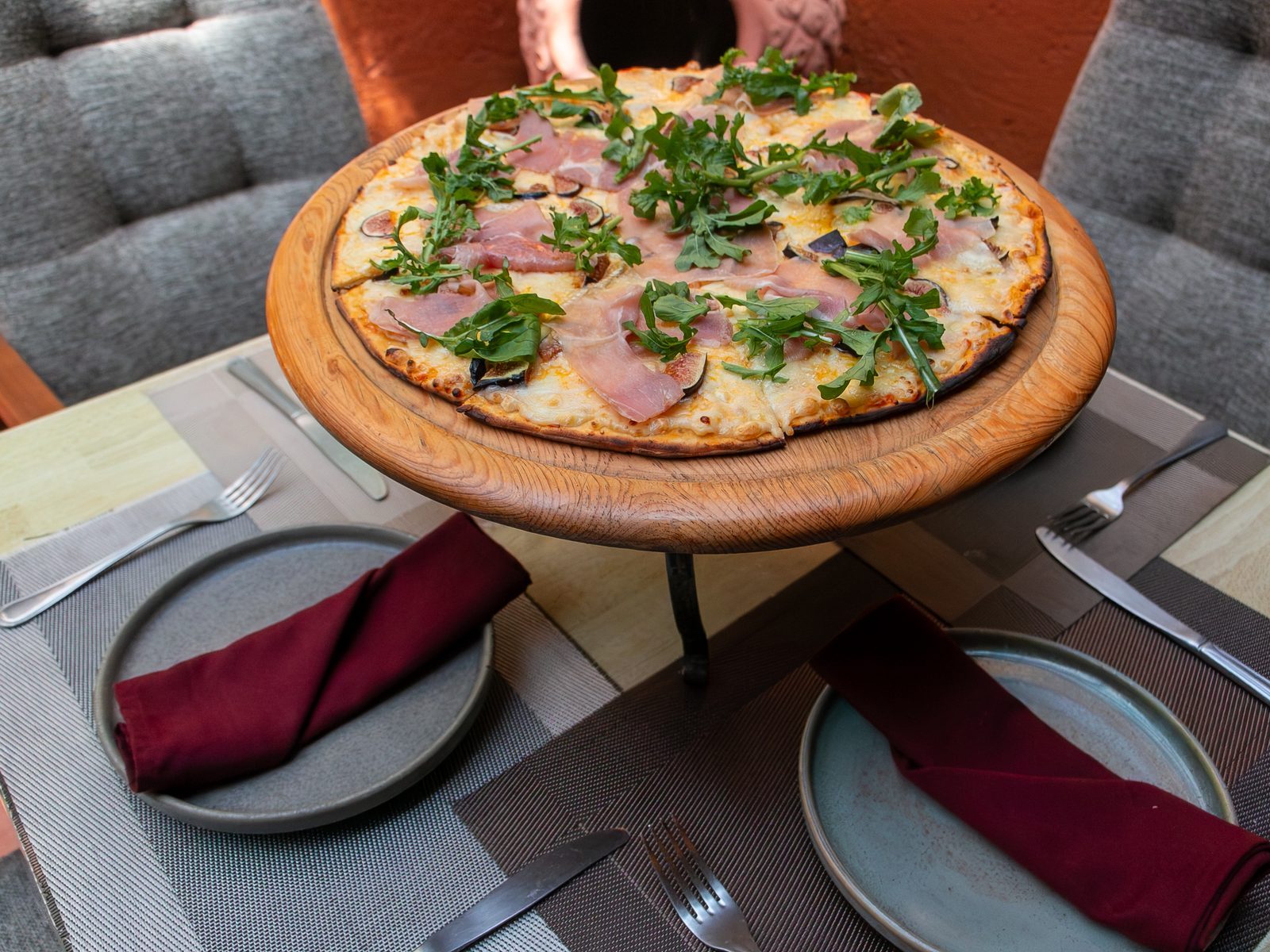 Mesa en la terraza con pizza de prosciutto y arúgula sobre base de madera elevada