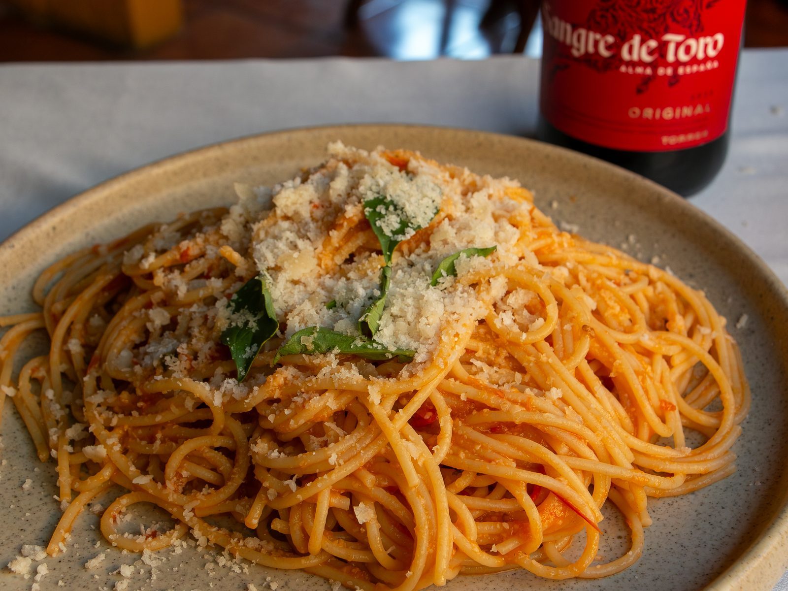 Plato de espagueti con salsa de tomate y parmesano rallado encima, junto a una botella de vino
