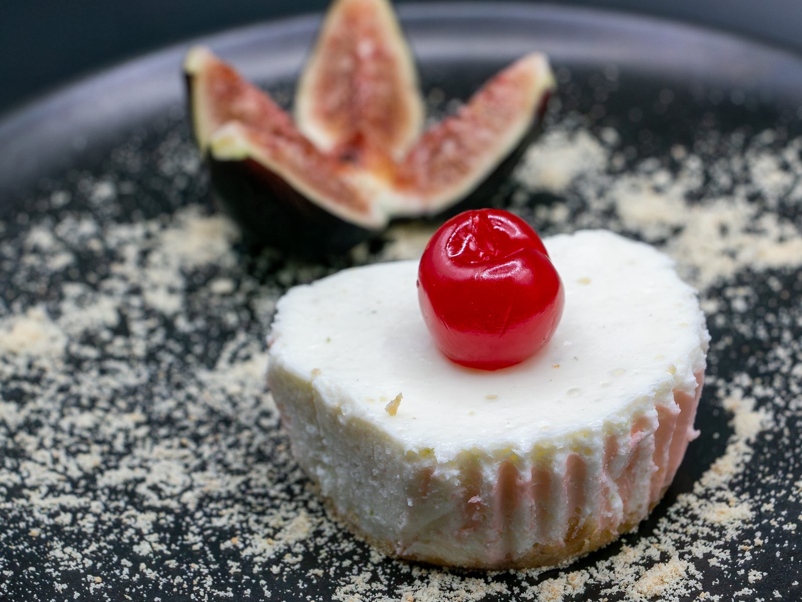 Cheesecake individual con cereza confitada en el centro y rebanadas de higo fresco al lado